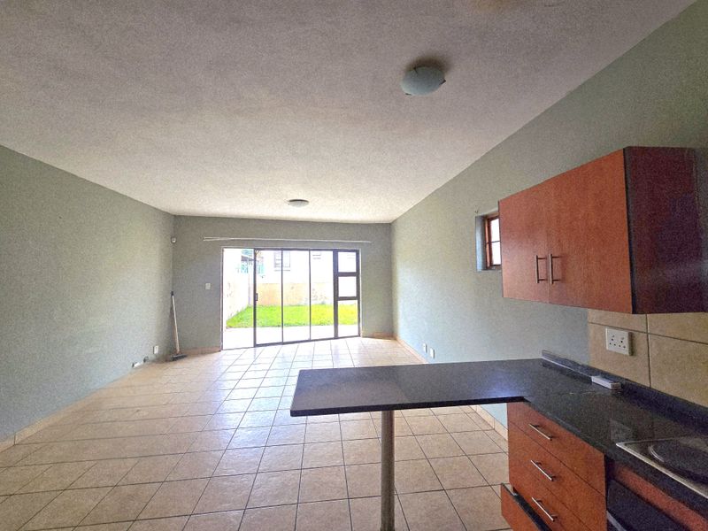 Spacious open-plan living and kitchen area featuring tiled floors, built-in cabinetry with granite countertops, and a sliding door leading to the rear garden.