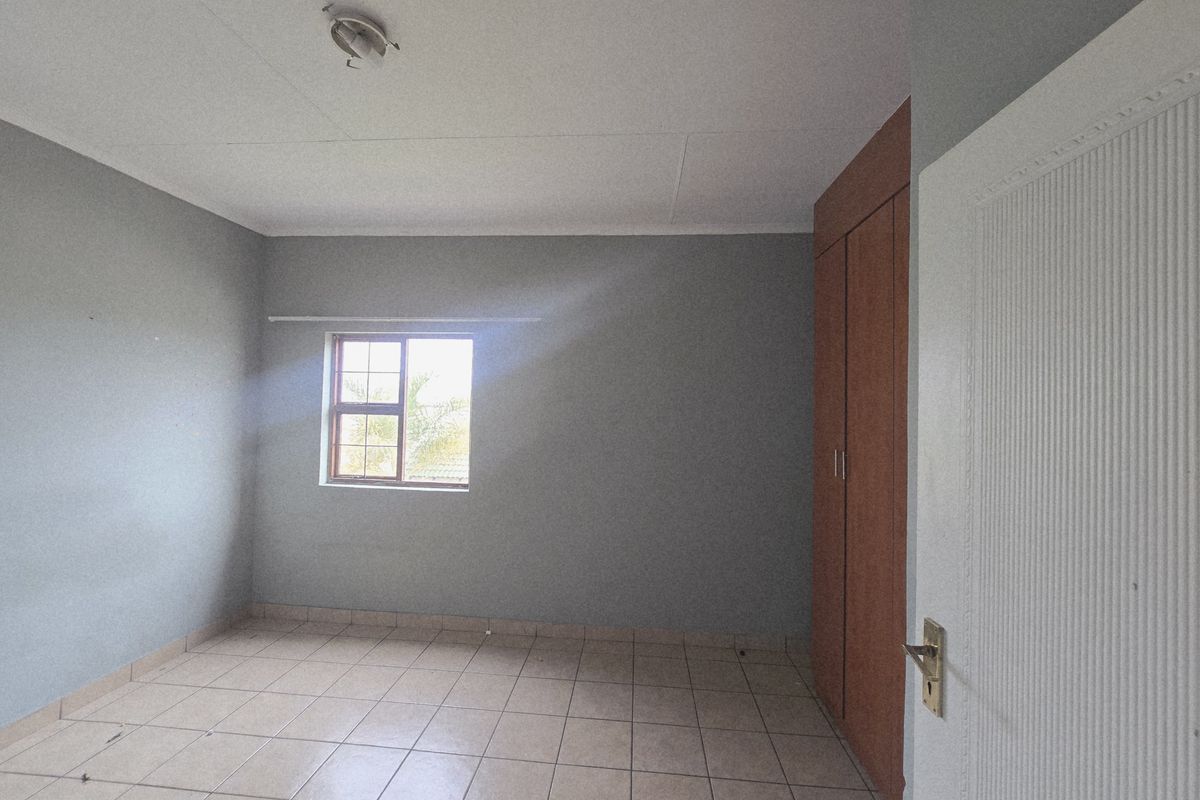A vacant bedroom featuring neutral grey walls, tiled flooring, and built-in wooden cupboards, offering a clean and versatile space.