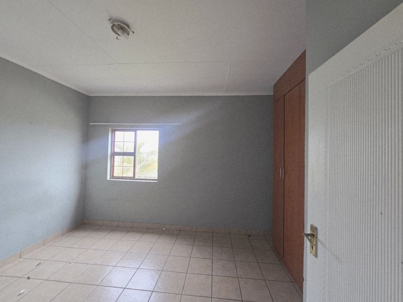 A vacant bedroom featuring neutral grey walls, tiled flooring, and built-in wooden cupboards, offering a clean and versatile space.