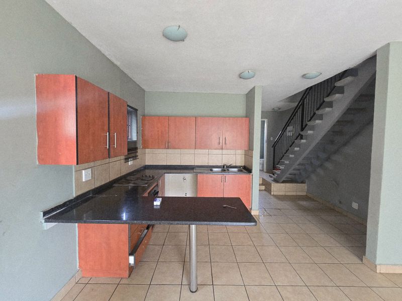 Open plan kitchen area featuring built-in cabinetry, dark countertops, and tiled flooring, adjacent to an internal staircase in a townhouse setting.