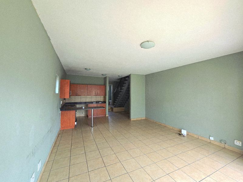An open-plan living and kitchen area featuring tiled flooring, built-in cabinetry, and a staircase leading to the upper level.