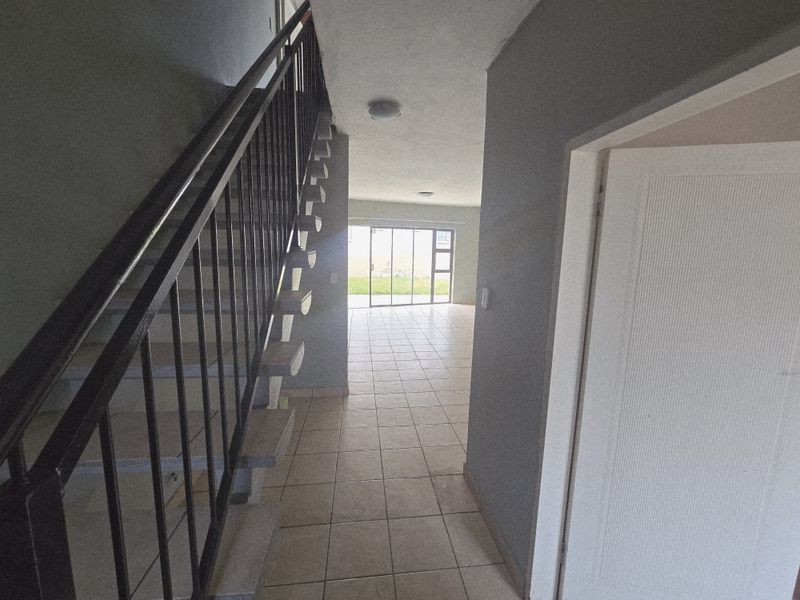 An open-plan hallway featuring a staircase with a metal balustrade, tiled flooring, and a sliding glass door leading to the rear outdoor area.