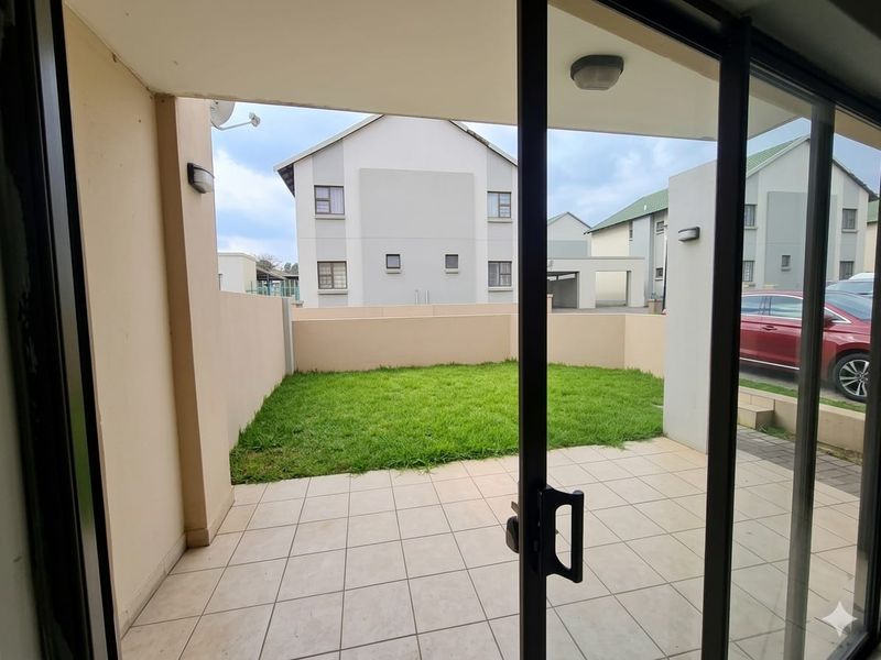 A covered patio area with tiled flooring, leading out to a private lawn and enclosed by boundary walls.