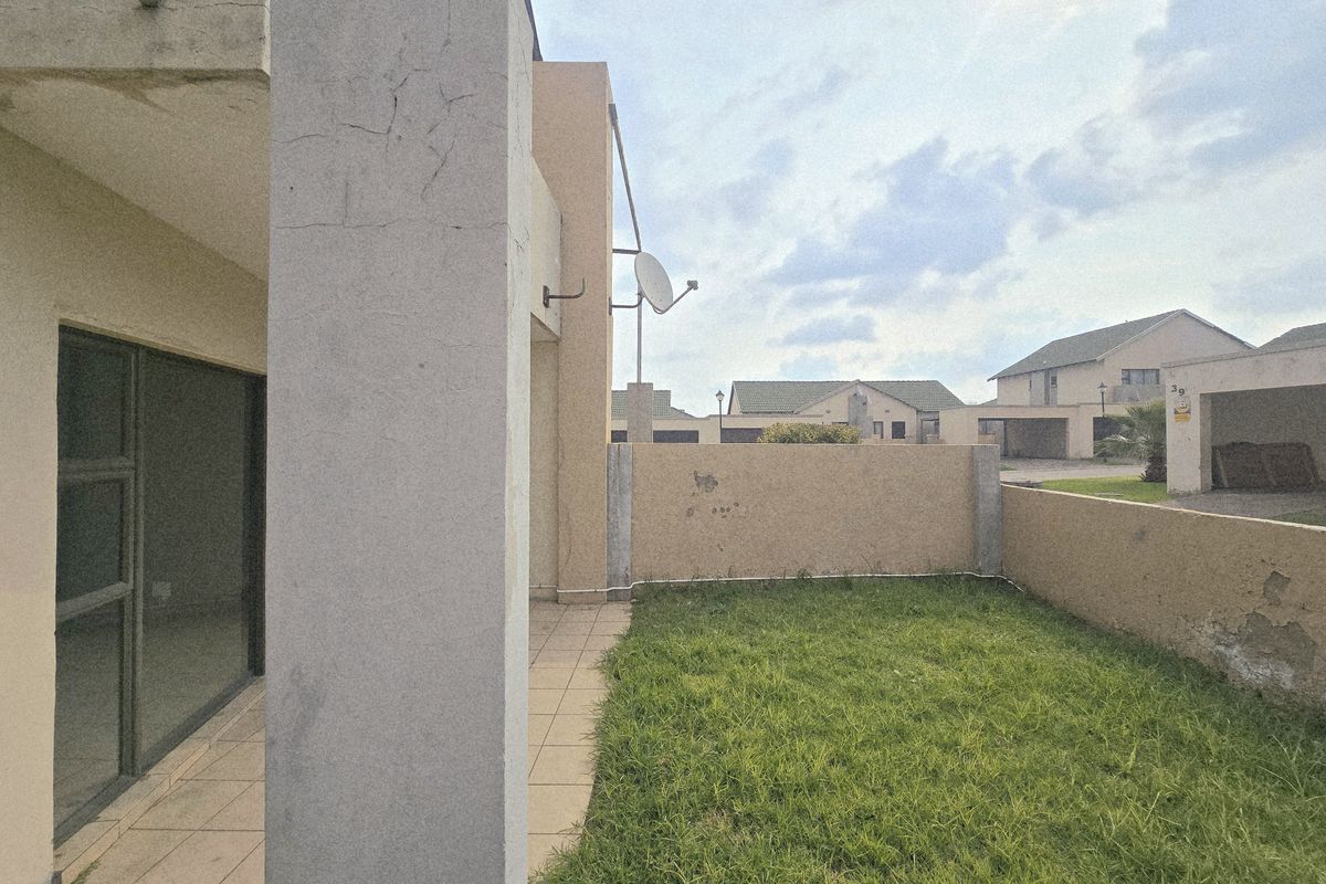Rear view of the townhouse featuring a small tiled patio, a private grassed garden area, and a boundary wall with visible exterior wear.