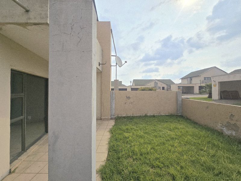 Rear view of the townhouse featuring a small tiled patio, a private grassed garden area, and a boundary wall with visible exterior wear.