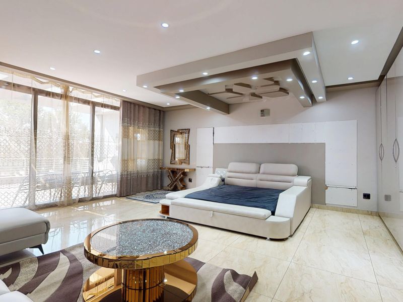 Spacious bedroom featuring a modern recessed ceiling with integrated lighting, large sliding glass doors, polished tile flooring, and extensive built-in wardrobe cabinetry.