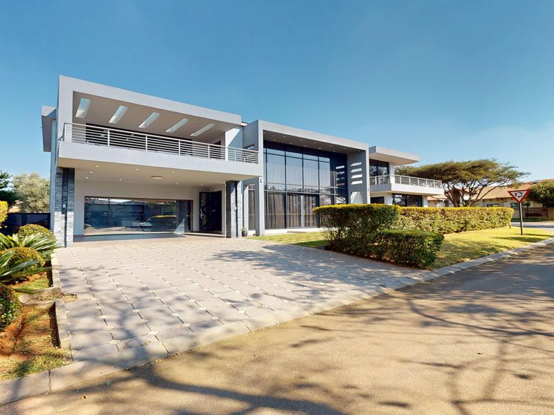 Modern double-story architectural home featuring a paved driveway, expansive glass facade, upper-level balconies, and a sleek contemporary design.