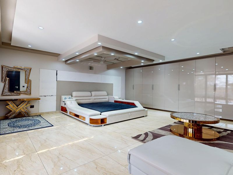 Spacious primary bedroom featuring high-gloss built-in cabinetry, recessed ceiling lighting with a decorative bulkhead, and polished marble-look floor tiles.