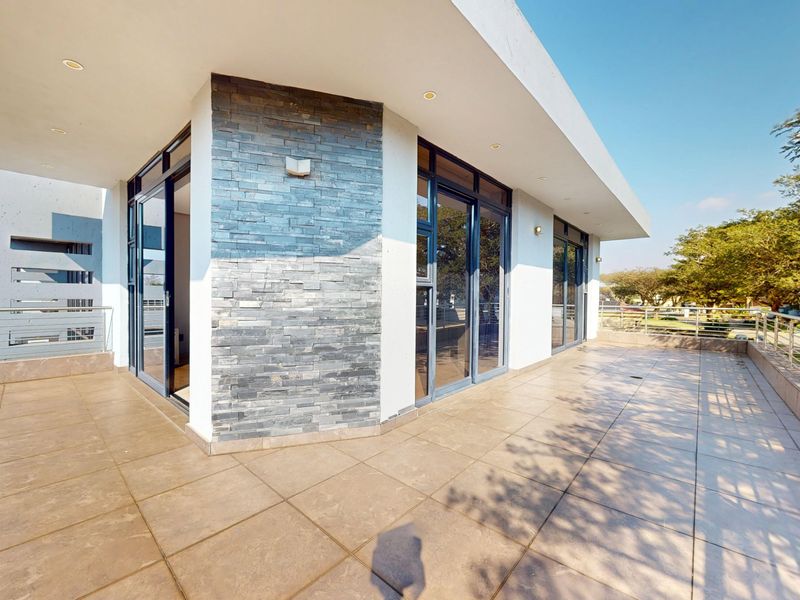Spacious covered balcony featuring modern tiled flooring, stone-clad feature wall, and sleek aluminum sliding doors providing seamless indoor-outdoor flow.