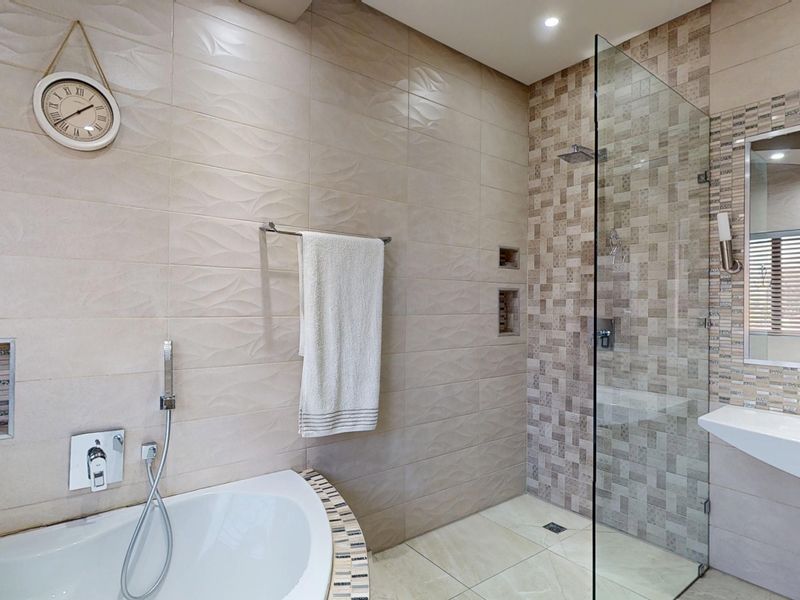 Modern bathroom featuring a built-in bathtub, a glass-enclosed walk-in shower with mosaic tile accents, and a wall-mounted vanity basin.