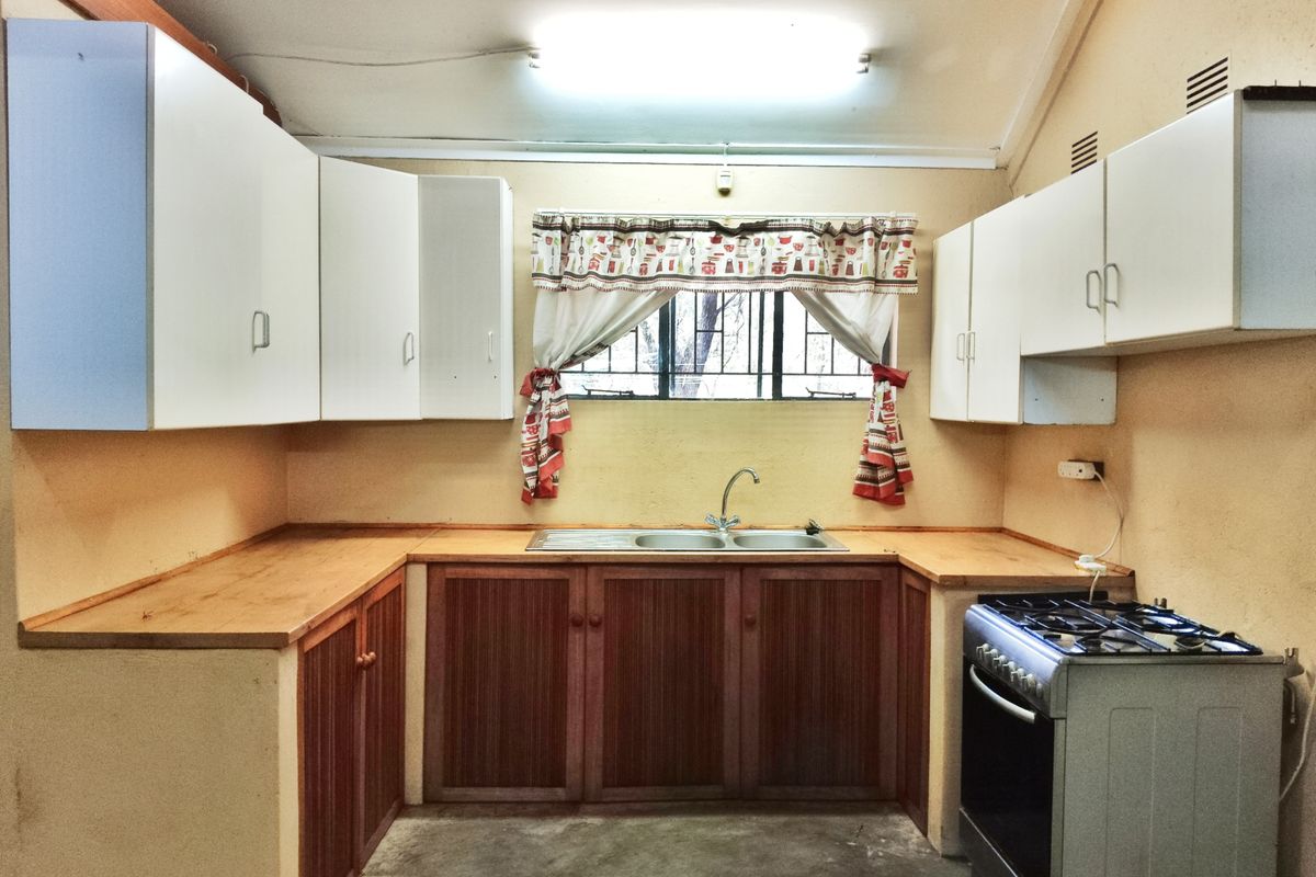 A functional kitchen featuring wooden cabinetry, double sink, and a freestanding gas stove, requiring cosmetic updates to modernize the space.