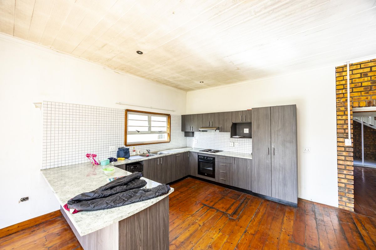 Kitchen featuring dark wood cabinetry, laminate countertops, built-in oven, hob, and extractor fan, with timber flooring and ceiling.