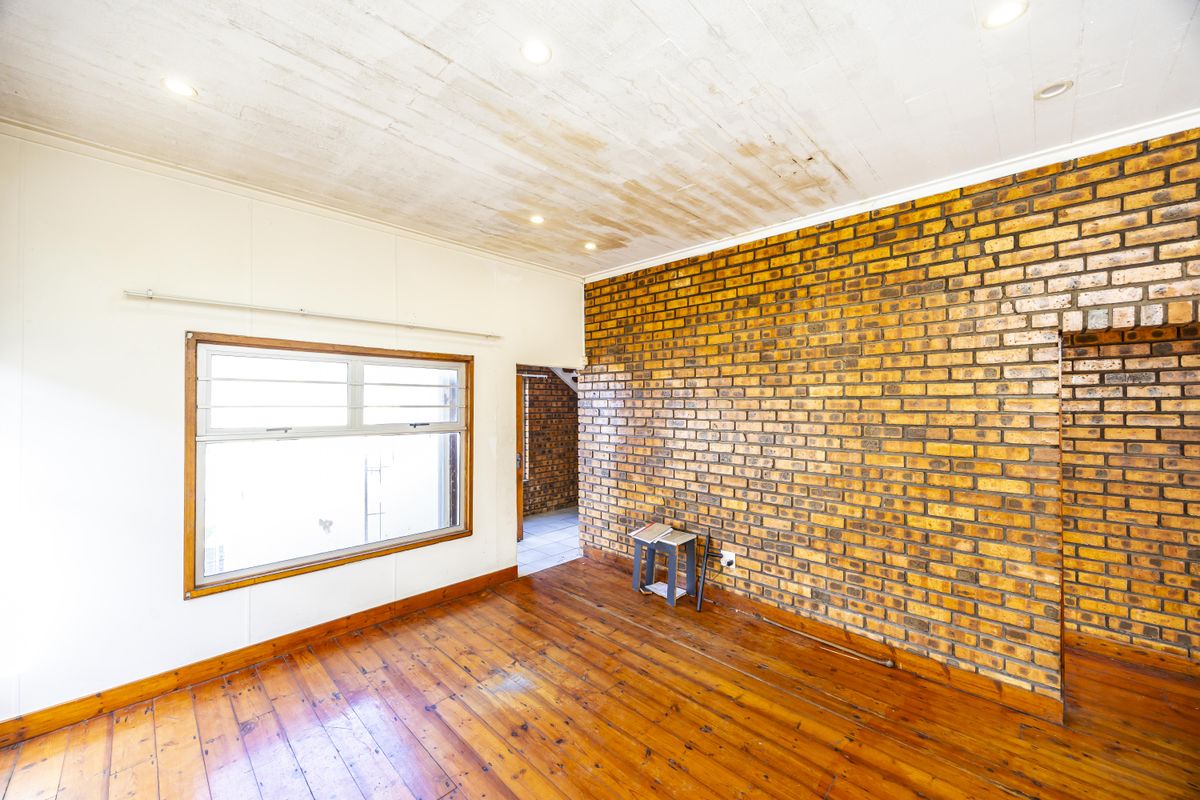 Living area featuring an exposed brick wall, polished timber flooring, and recessed lighting, showing signs of ceiling water damage and wear.