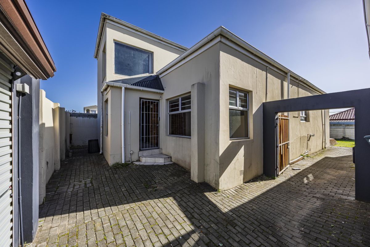 Rear exterior view of the property featuring a paved courtyard, security gate, and access to the side of the house.
