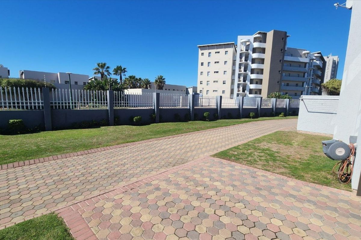A well-maintained paved driveway and lawn area enclosed by a perimeter wall and metal fencing within a townhouse complex.