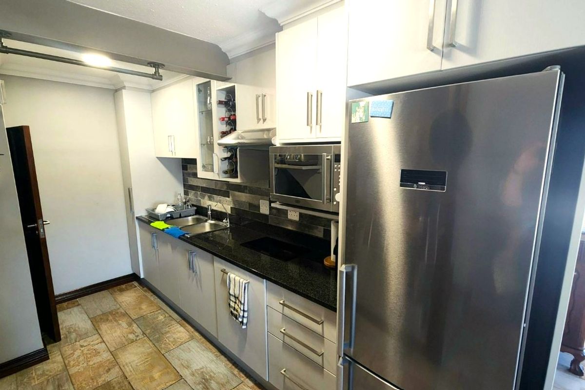 Modern kitchen featuring sleek white cabinetry, dark granite countertops, integrated microwave, and extractor fan, complemented by durable tiled flooring.