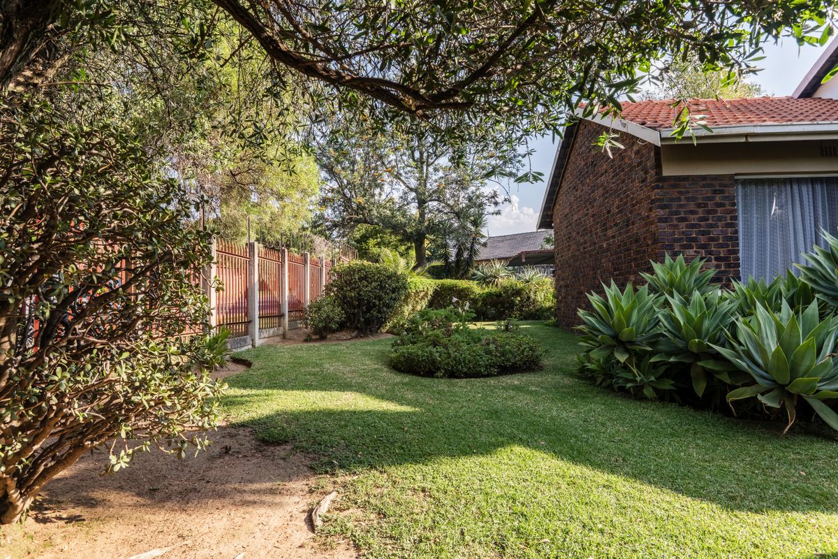 A well-maintained rear garden featuring a brick exterior wall, tiled roof, and established landscaping with metal perimeter fencing.