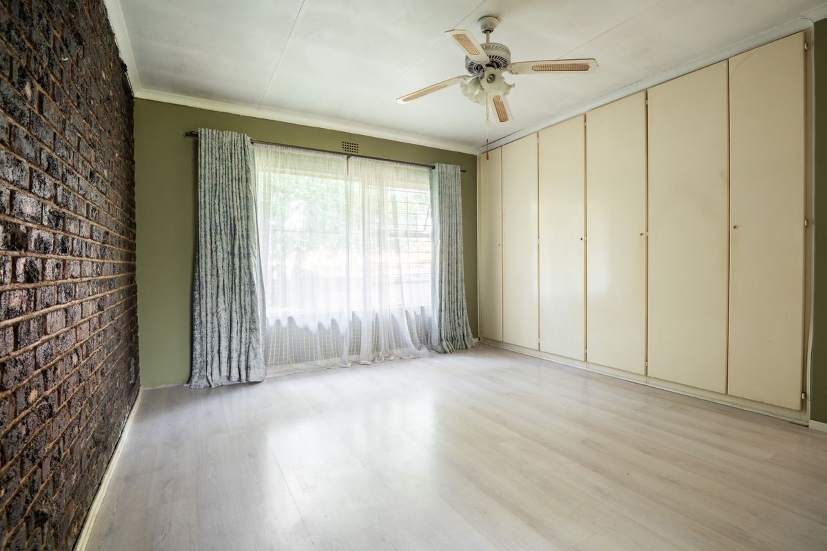 Spacious bedroom featuring an exposed brick feature wall, built-in cupboards, ceiling fan, and light-toned laminate flooring.