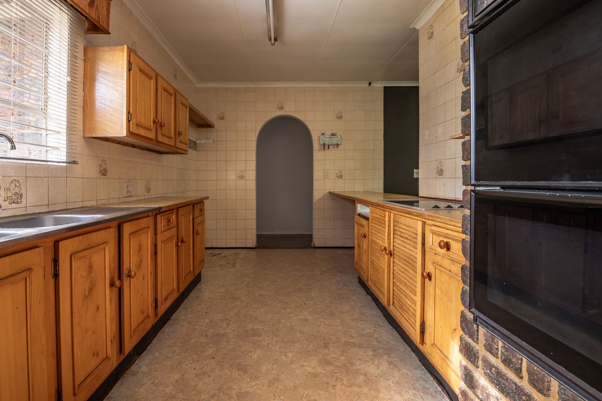 A dated kitchen featuring wooden cabinetry, built-in oven, hob, and tiled splashbacks, offering a blank canvas for a modern renovation.