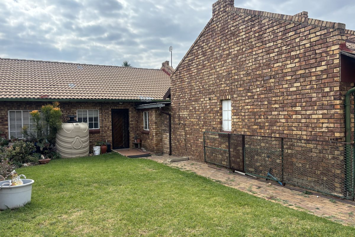 Rear view of the townhouse featuring a face brick exterior, tiled roof, paved walkway, and a private garden area with a water storage tank.