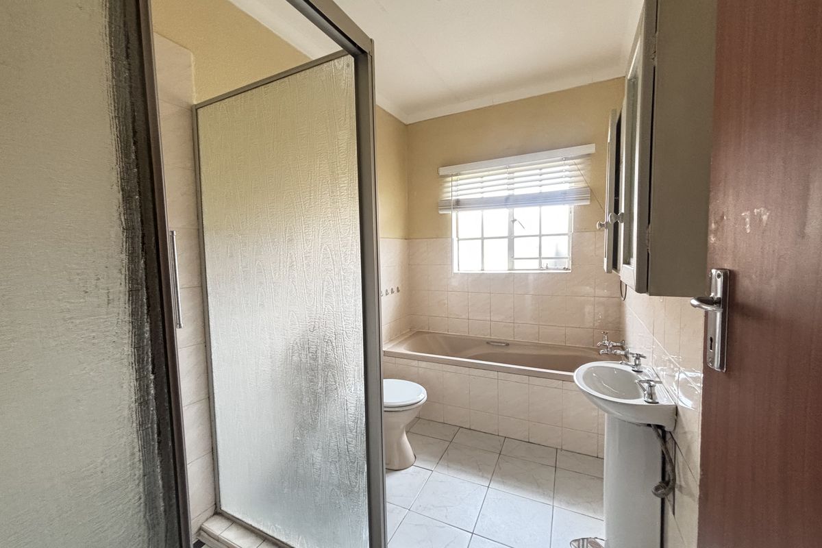 A functional bathroom featuring a pedestal basin, built-in bathtub, and a separate shower enclosure with tiled finishes.
