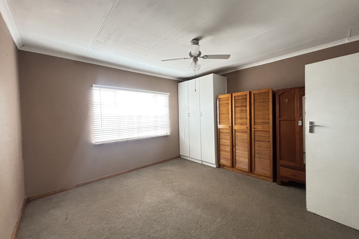 A bedroom featuring a ceiling fan, built-in wardrobe, and venetian blinds, requiring cosmetic updates to the flooring and ceiling.