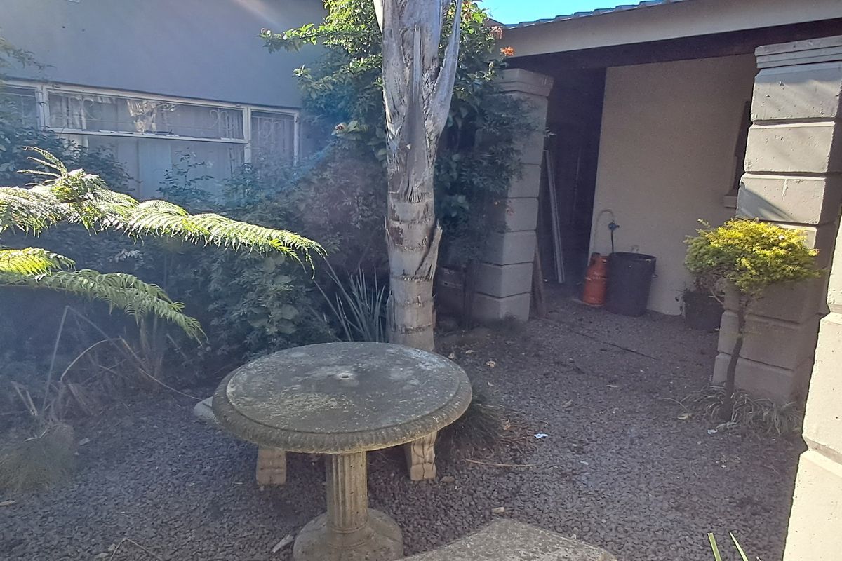 A rear outdoor patio area featuring a covered section, gravel flooring, and established garden landscaping.