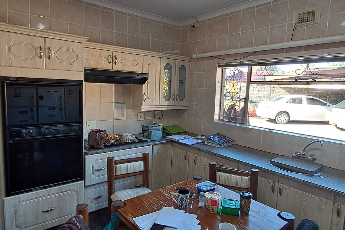 A functional kitchen featuring built-in cabinetry, a wall-mounted oven, extractor fan, and a tiled backsplash with a large window overlooking the exterior.