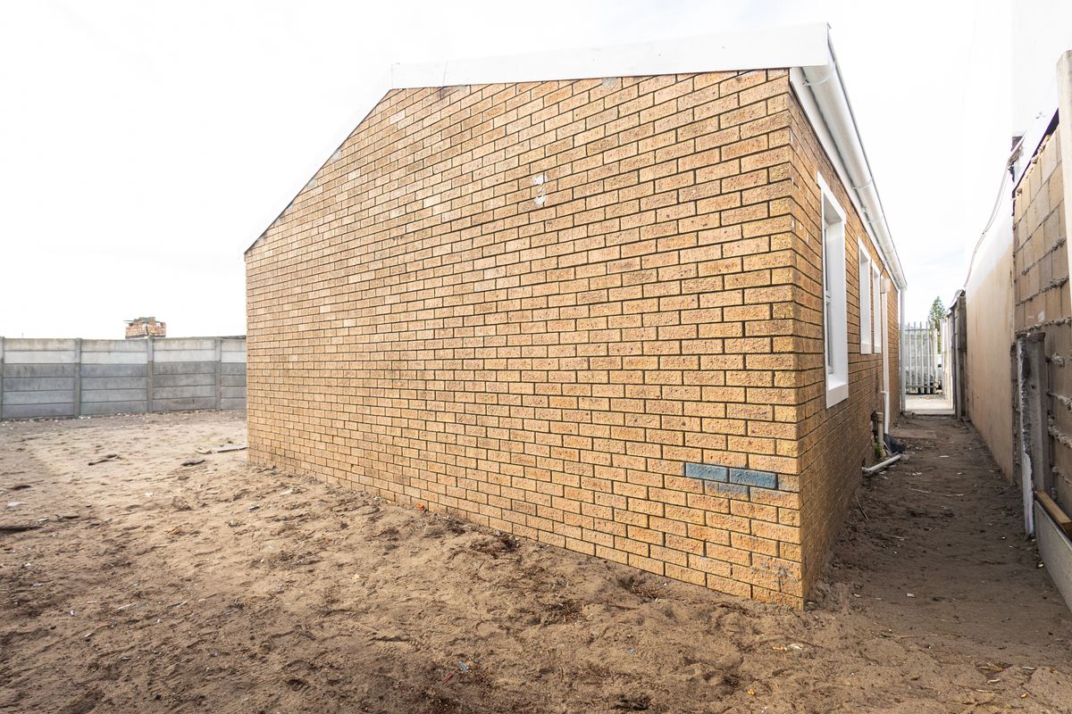 Rear view of the property showing the face brick exterior wall, guttering, and surrounding unlandscaped yard area.