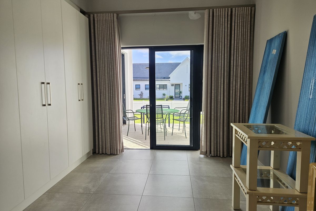 A bright living area featuring large format floor tiles, floor-to-ceiling built-in cabinetry, and sliding glass doors opening onto an outdoor patio.