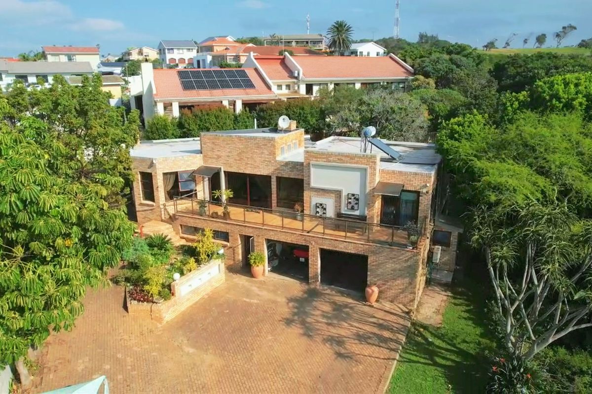 Aerial view of a multi-level brick house featuring a spacious balcony, double garage, paved driveway, and integrated solar energy systems.