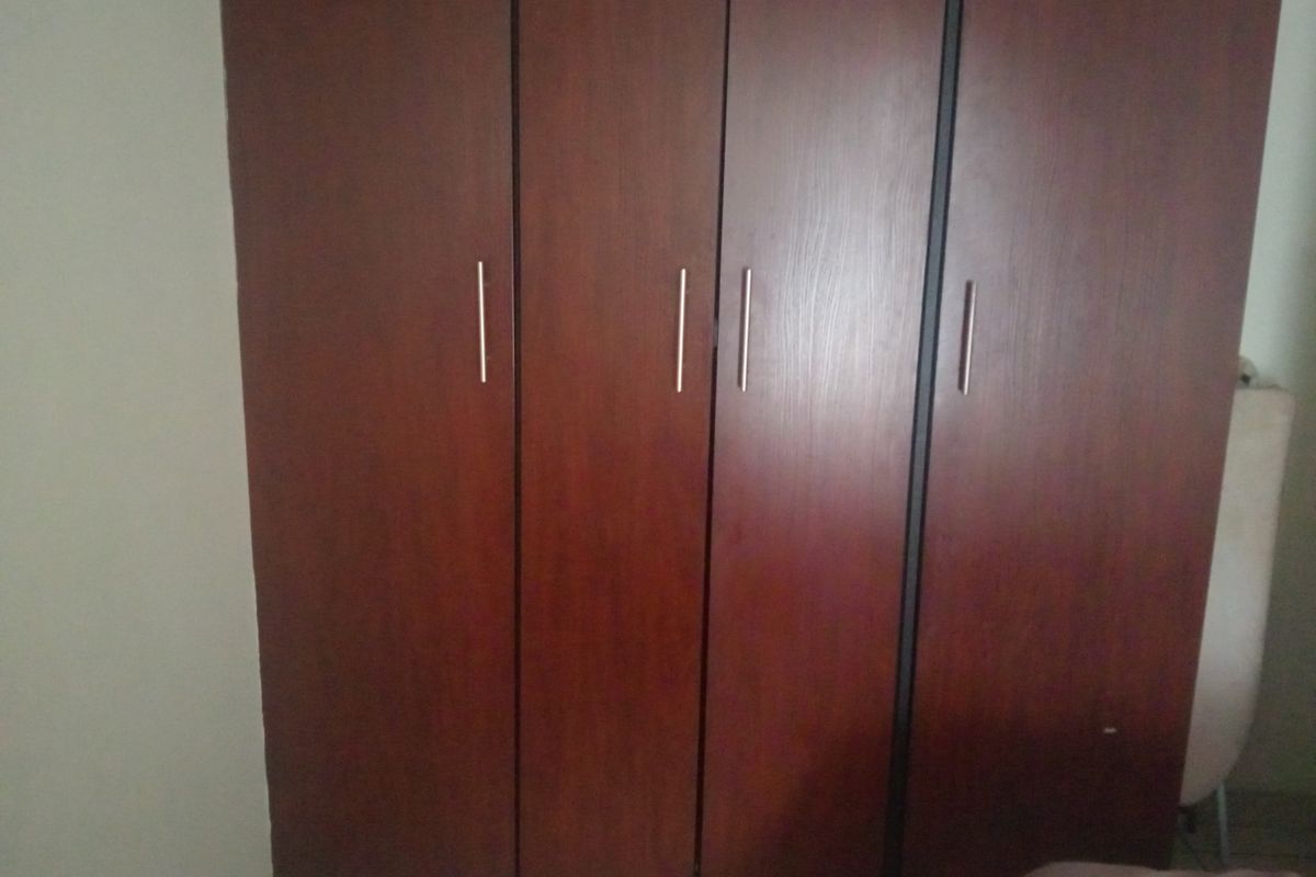 A bedroom featuring a dark wood-finish built-in wardrobe with modern metal handles.