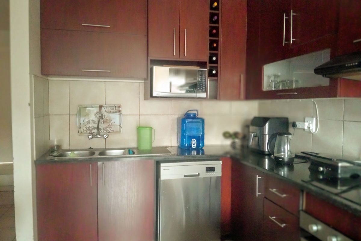 A functional kitchen featuring dark wood cabinetry, granite countertops, a double sink, and integrated appliances including a microwave and extractor fan.