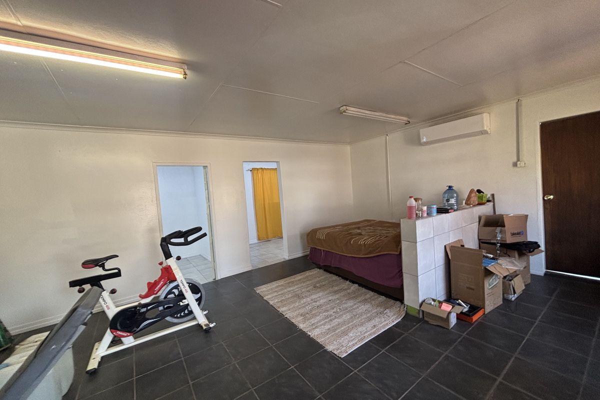 A spacious bedroom featuring tiled flooring, a split-system air conditioner, and a tiled partition wall, offering a functional layout with direct access to adjacent rooms.