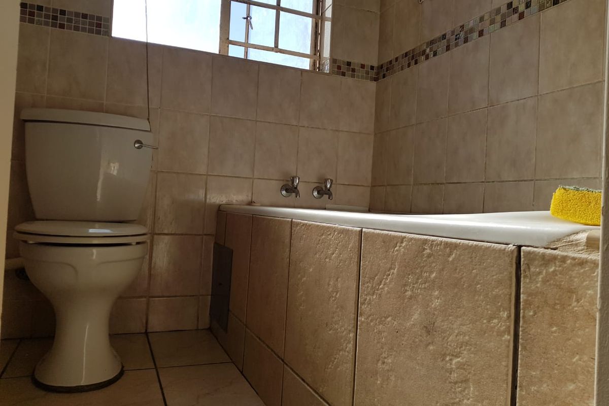 A functional bathroom featuring a built-in bathtub, standard toilet, and neutral ceramic wall and floor tiling throughout.
