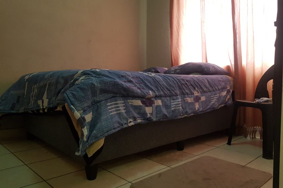 A bedroom featuring tiled flooring and natural light from a window with curtains.