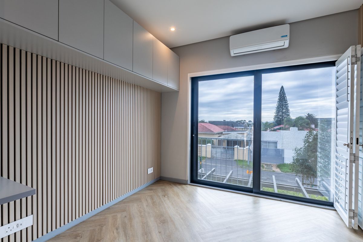 Modern bedroom featuring timber slat wall paneling, herringbone flooring, built-in overhead storage, and a split-system air conditioner with access to a balcony.