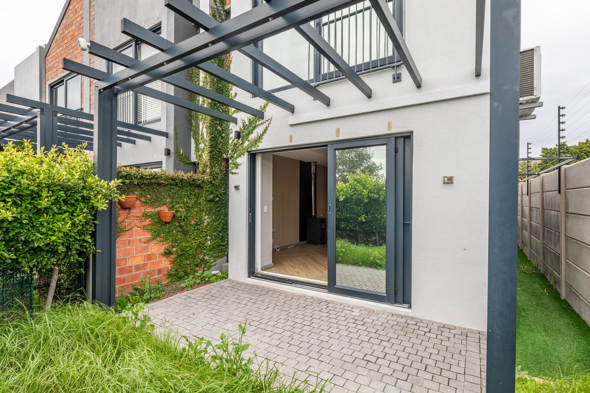 Rear exterior view of the townhouse featuring a paved patio, modern pergola structure, and sliding glass doors leading into the living area.