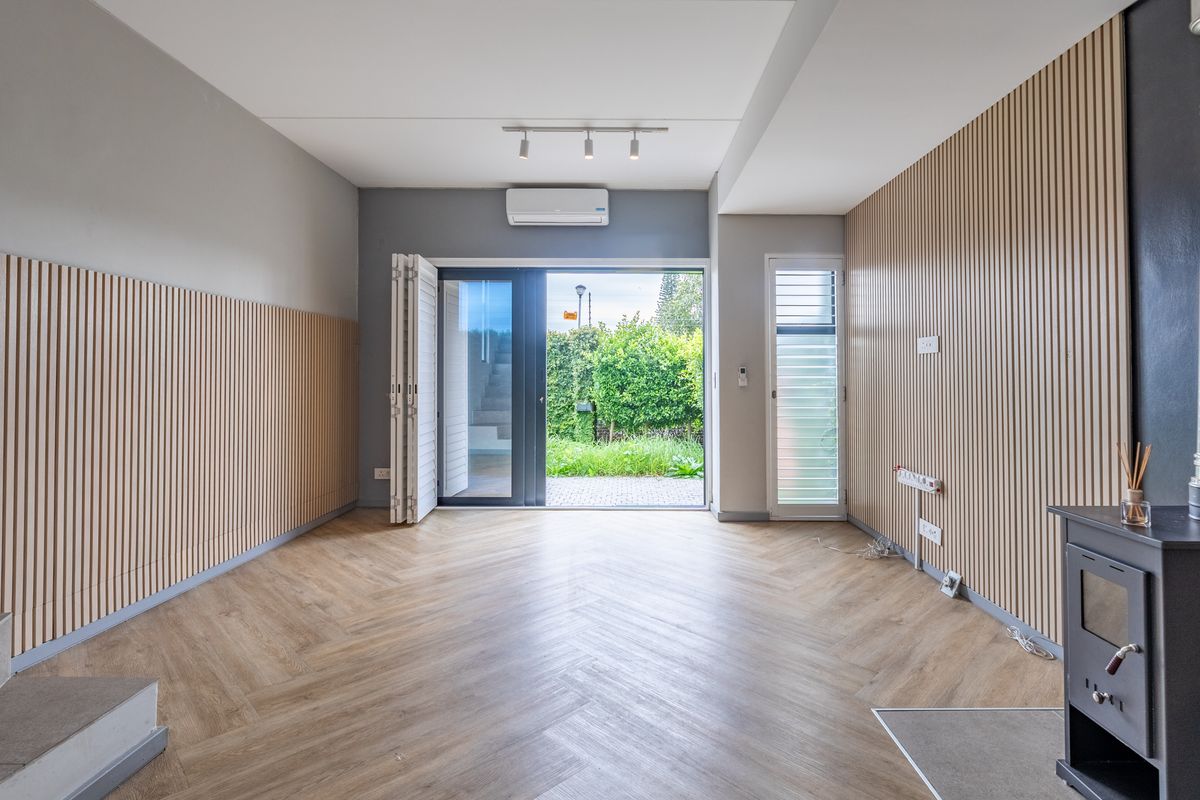 Spacious living area featuring modern timber slat wall paneling, herringbone flooring, a wood-burning fireplace, and seamless access to the rear garden through bi-fold doors.