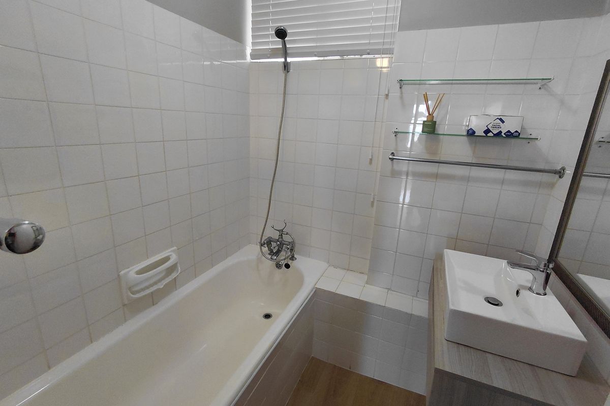 A functional bathroom featuring a white bathtub with handheld shower fixture, a modern vessel sink on a vanity, and tiled wall finishes.