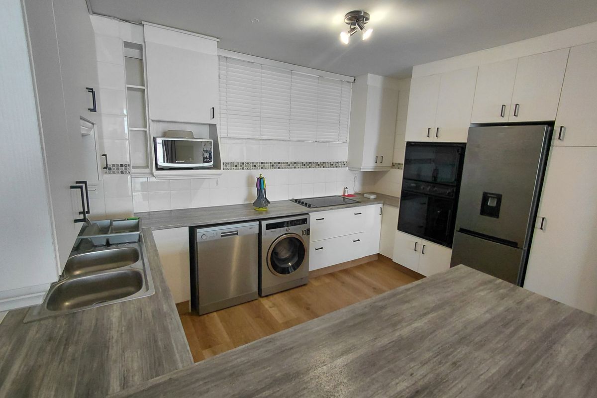 A functional kitchen featuring white cabinetry, wood-look laminate countertops, a double sink, and integrated stainless steel appliances including an oven and hob.