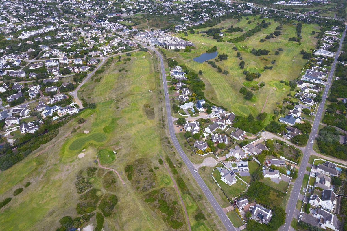 An aerial view of a residential estate featuring a golf course, surrounding homes, and established road infrastructure.