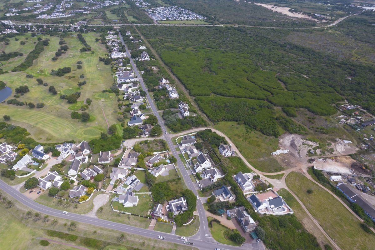 An aerial view of a residential estate featuring paved roads, established housing, and proximity to a golf course and natural coastal landscape.