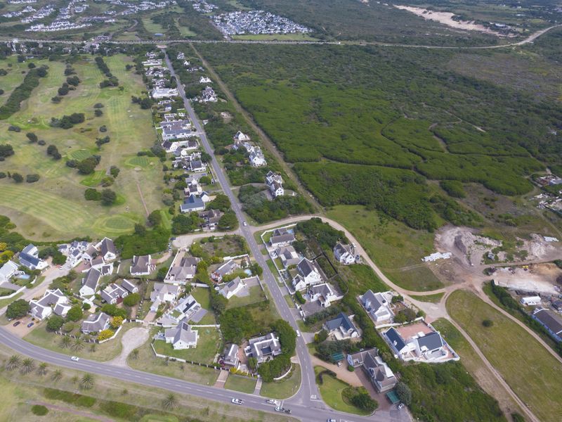 An aerial view of a residential estate featuring paved roads, established housing, and proximity to a golf course and natural coastal landscape.