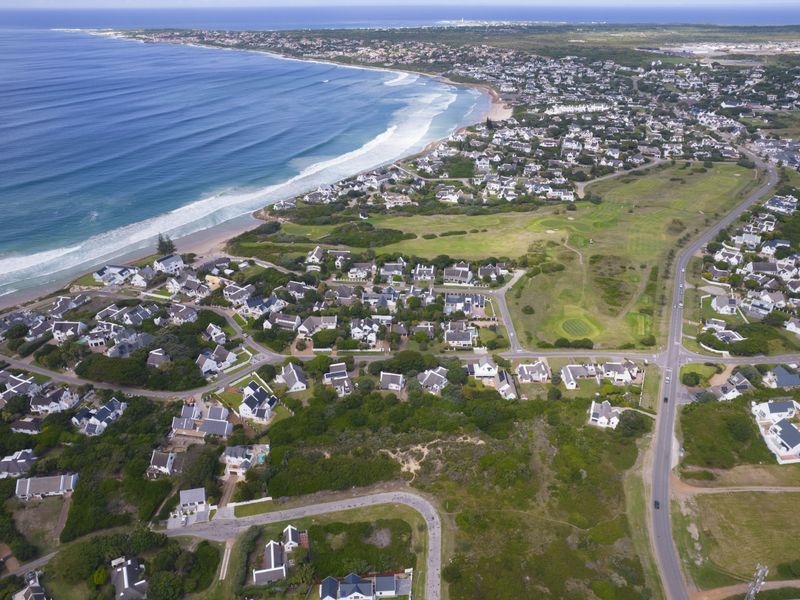 An expansive aerial view of a coastal residential estate, showcasing proximity to the beach, surrounding greenery, and local golf course infrastructure.