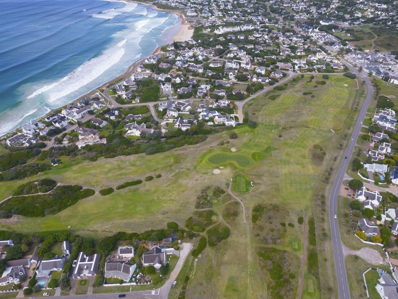 An aerial view of a coastal residential area featuring a golf course and proximity to the ocean.