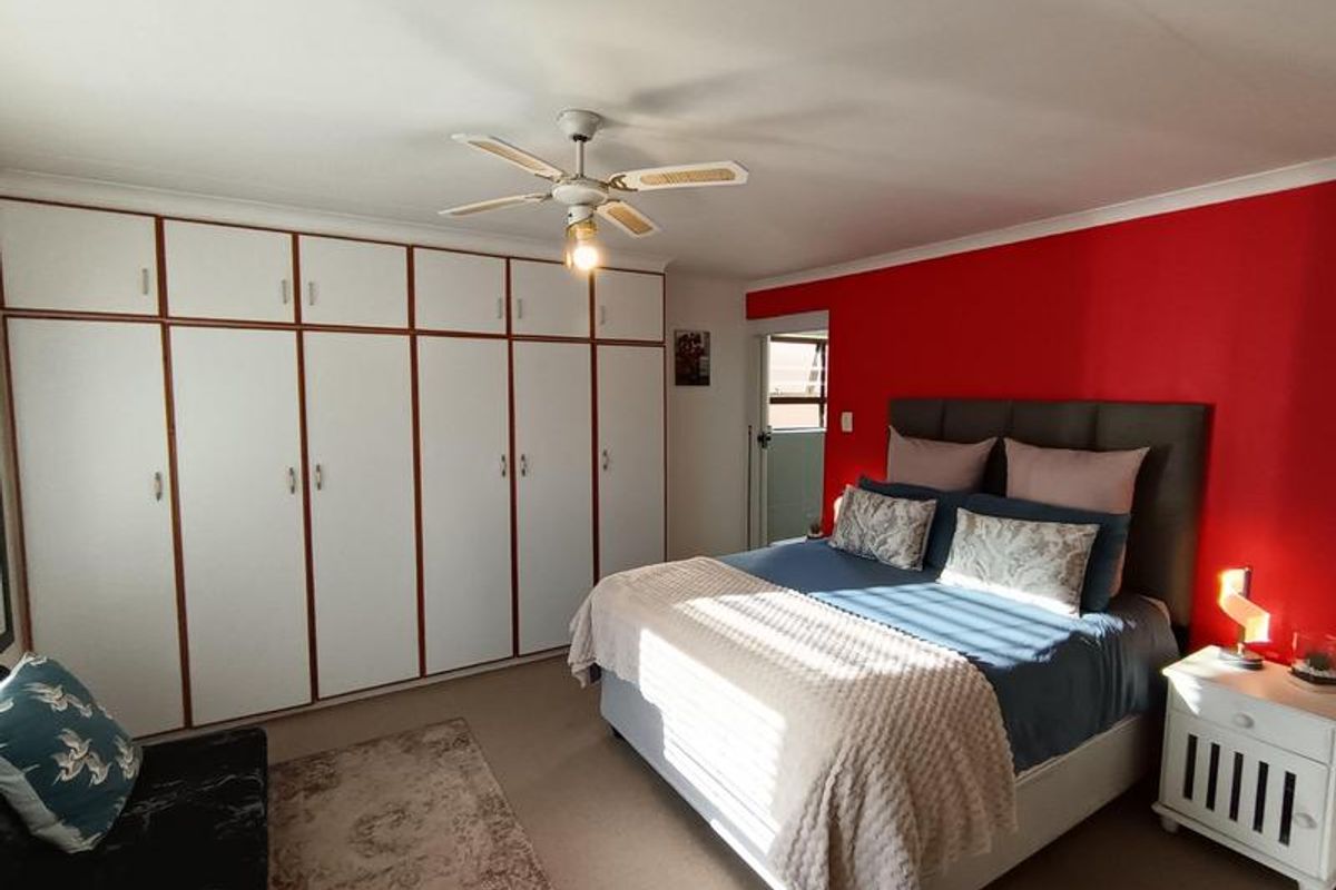 A spacious bedroom featuring extensive built-in cabinetry with white doors and a ceiling fan, complemented by a bold red accent wall.