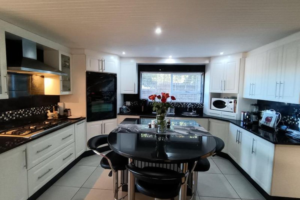 Modern kitchen featuring white cabinetry, black granite countertops, a central island with seating, built-in oven, gas hob, and stainless steel extractor fan.