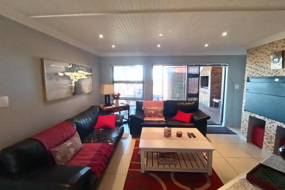 Spacious living room featuring tiled flooring, recessed ceiling lighting, and a built-in fireplace with stone cladding, leading out to a covered patio area.