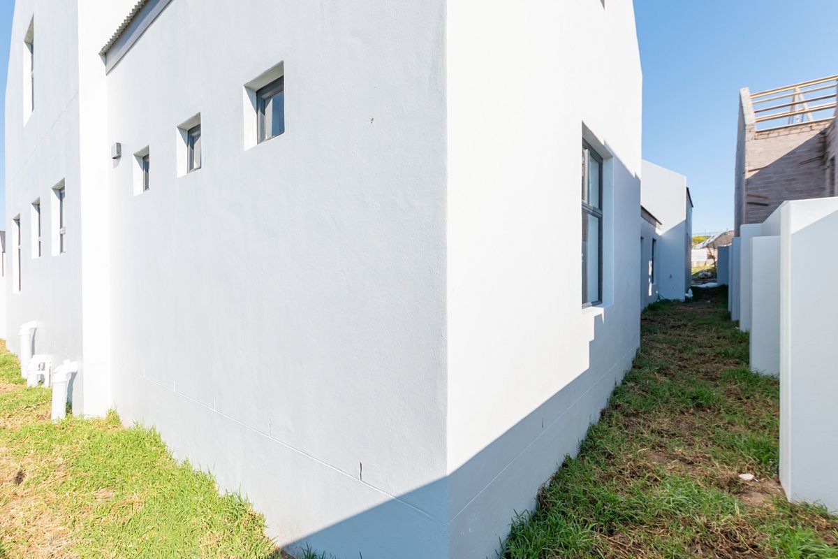 Side and rear view of a modern white plastered house featuring aluminium window frames and unfinished garden area.